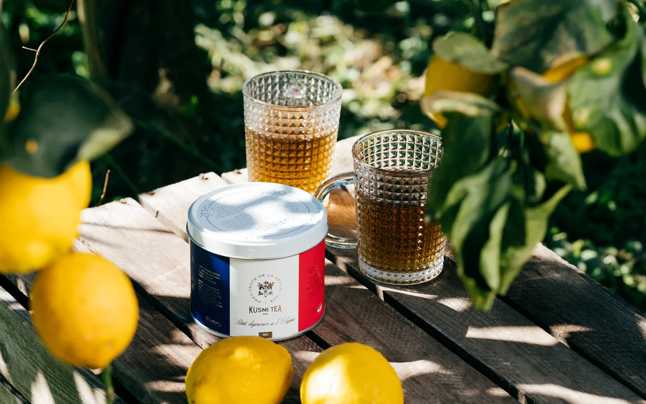 Boîte de thé Kusmi Tea et verres de thé sur une table en bois, entre des citrons, en plein soleil